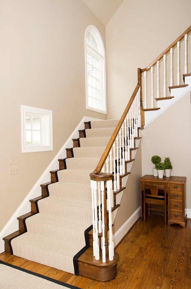 Aménagement d'un grand escalier classique en L avec des marches en moquette, des contremarches en bois et un garde-corps en bois.