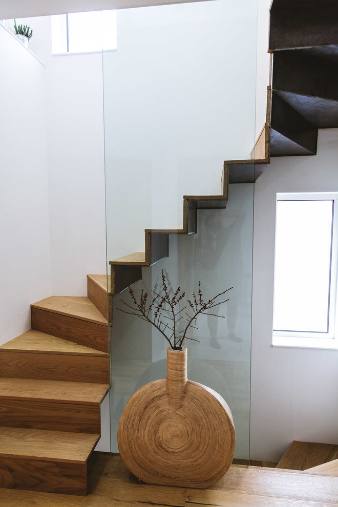 На фото: изогнутая деревянная лестница в современном стиле с деревянными ступенями и стеклянными перилами