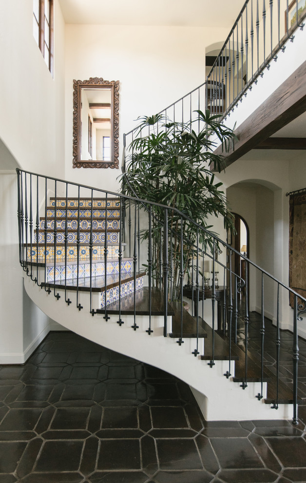 Modelo de escalera curva mediterránea con escalones de madera, contrahuellas con baldosas y/o azulejos y barandilla de metal
