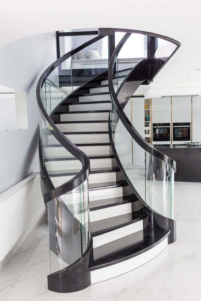 Aménagement d'un grand escalier courbe moderne avec des marches en bois, des contremarches en bois et un garde-corps en verre.