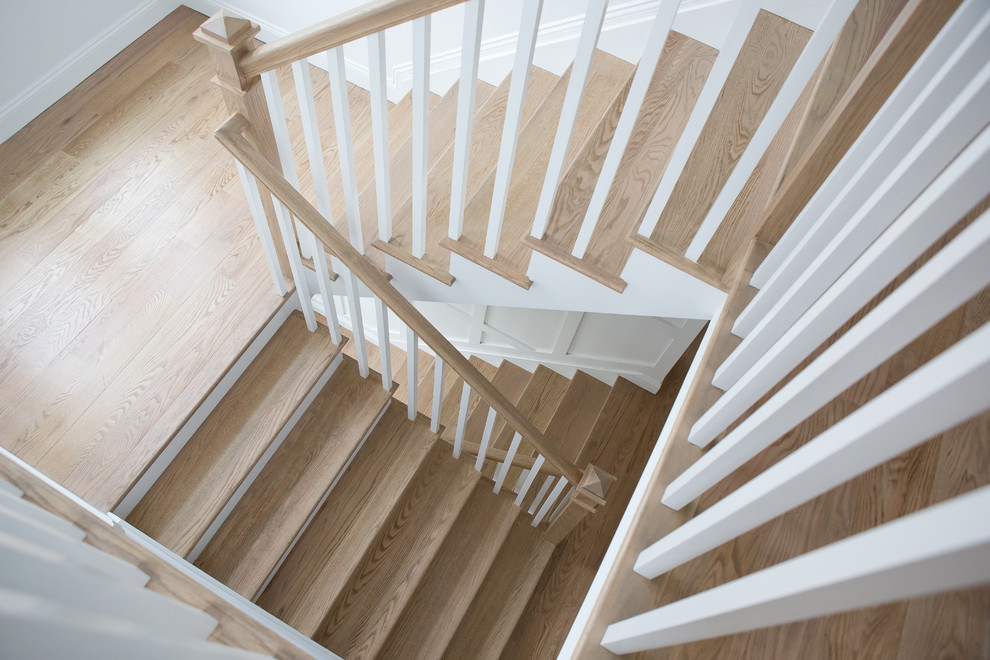 Стильный дизайн: большая угловая лестница в стиле неоклассика (современная классика) с деревянными ступенями, крашенными деревянными подступенками и деревянными перилами - последний тренд