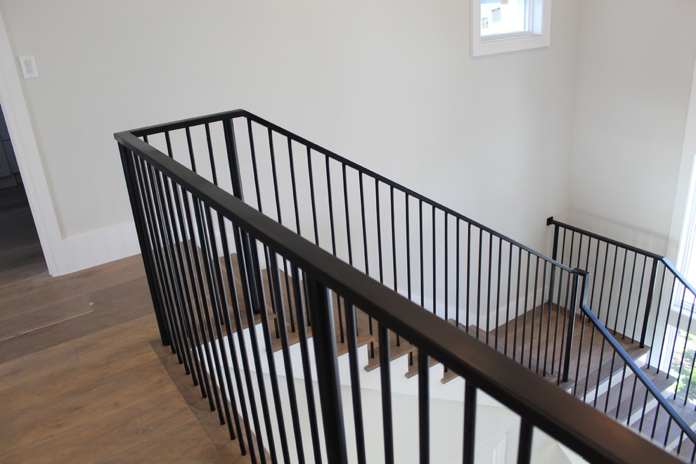 Idée de décoration pour un escalier tradition en L de taille moyenne avec des marches en bois, des contremarches en bois et un garde-corps en métal.