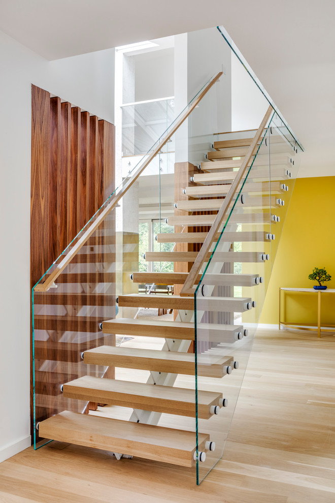 Пример оригинального дизайна: большая прямая лестница в современном стиле с деревянными ступенями и стеклянными перилами без подступенок