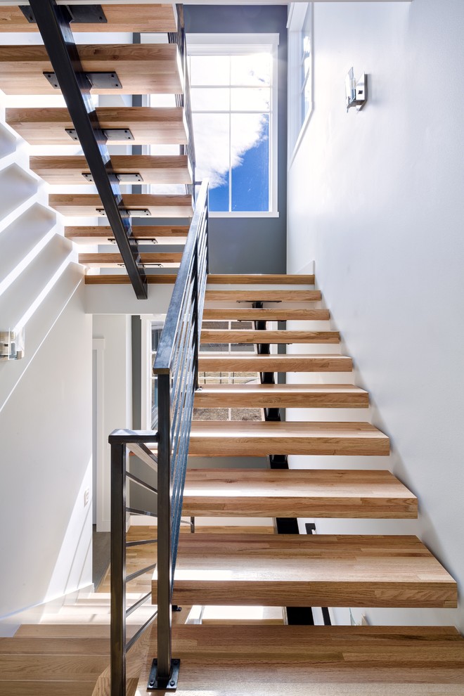 Стильный дизайн: большая лестница на больцах в стиле неоклассика (современная классика) с деревянными ступенями и металлическими перилами без подступенок - последний тренд