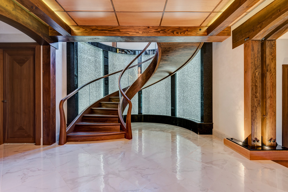 Imagen de escalera de caracol actual grande con escalones de madera, contrahuellas de madera y barandilla de vidrio
