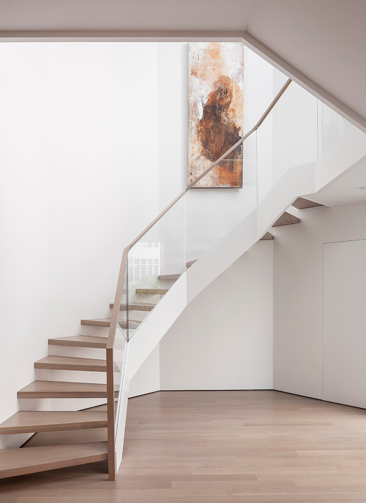 Ejemplo de escalera curva actual sin contrahuella con escalones de madera y barandilla de vidrio