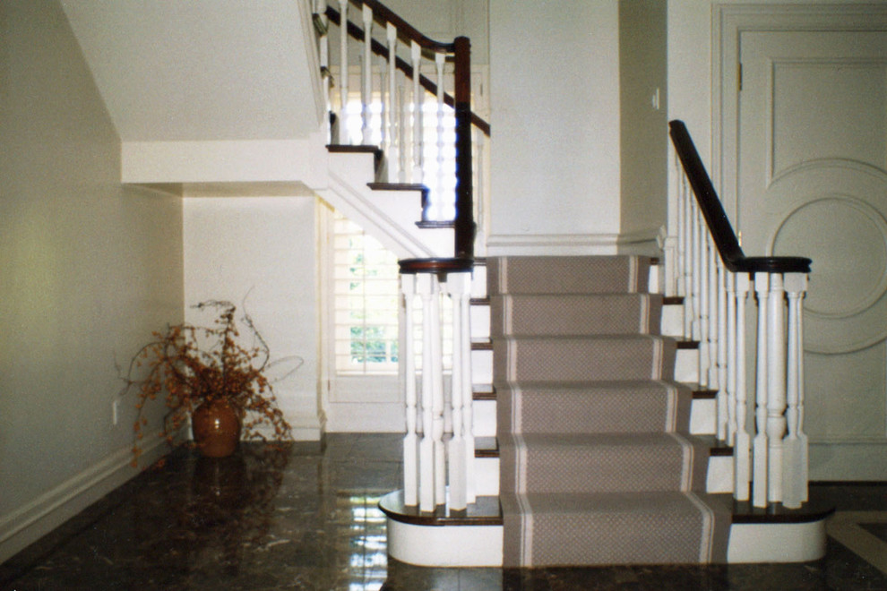 На фото: большая угловая лестница в классическом стиле с деревянными ступенями, крашенными деревянными подступенками и деревянными перилами с
