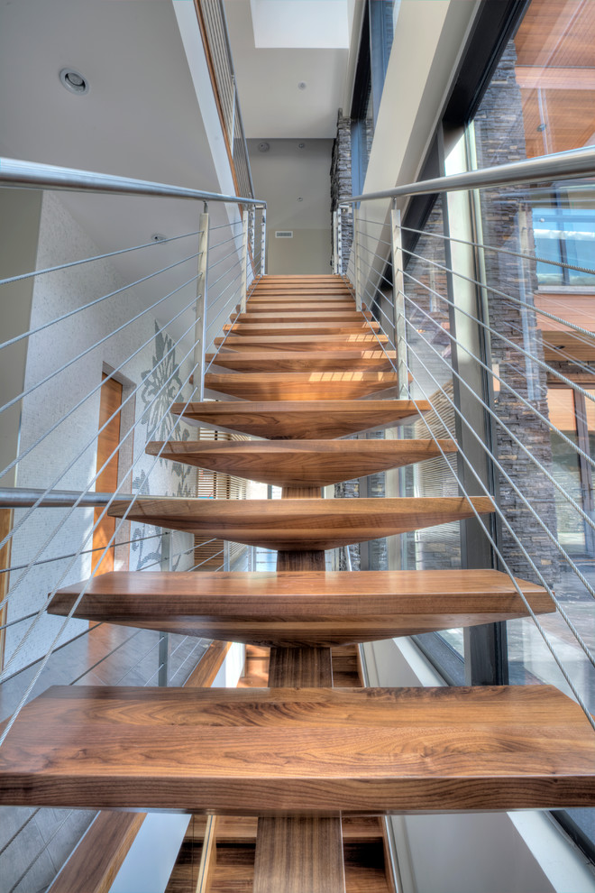 Cette photo montre un grand escalier sans contremarche droit tendance avec des marches en bois et un garde-corps en câble.