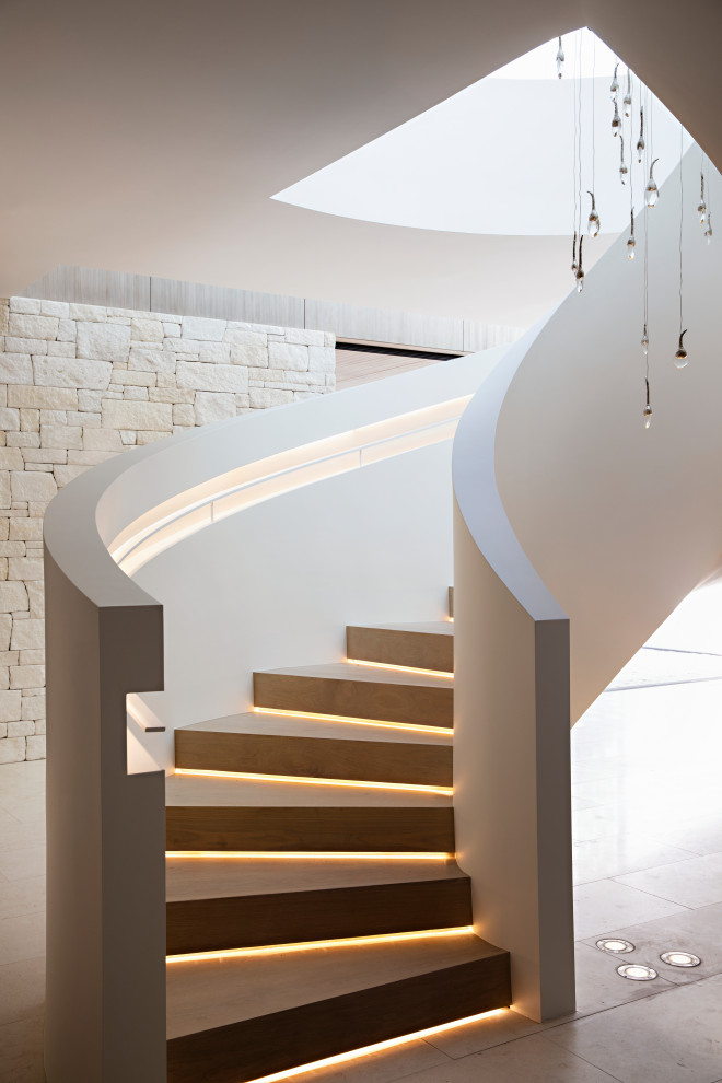 Imagen de escalera curva contemporánea con escalones de madera, contrahuellas de madera y barandilla de metal