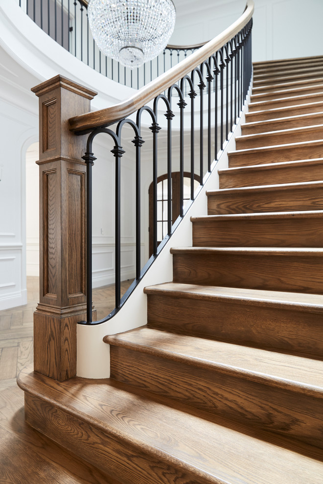На фото: огромная изогнутая деревянная лестница в классическом стиле с деревянными ступенями и деревянными перилами с