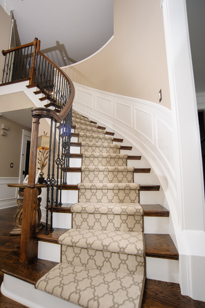 На фото: изогнутая лестница в стиле неоклассика (современная классика) с деревянными ступенями и ковровыми подступенками
