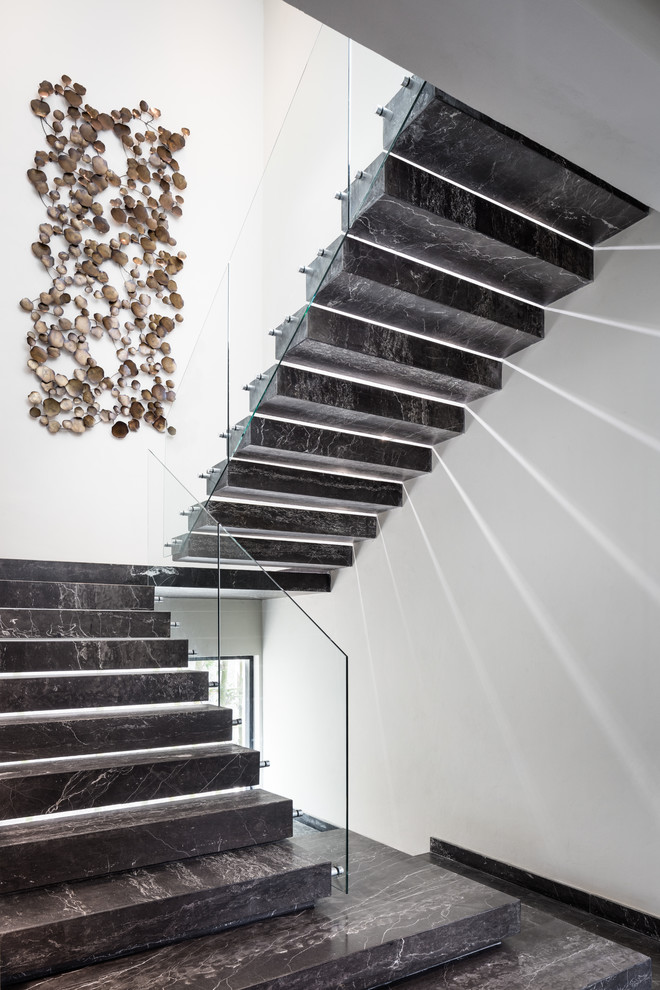 Стильный дизайн: лестница на больцах в современном стиле с стеклянными перилами и мраморными ступенями без подступенок - последний тренд