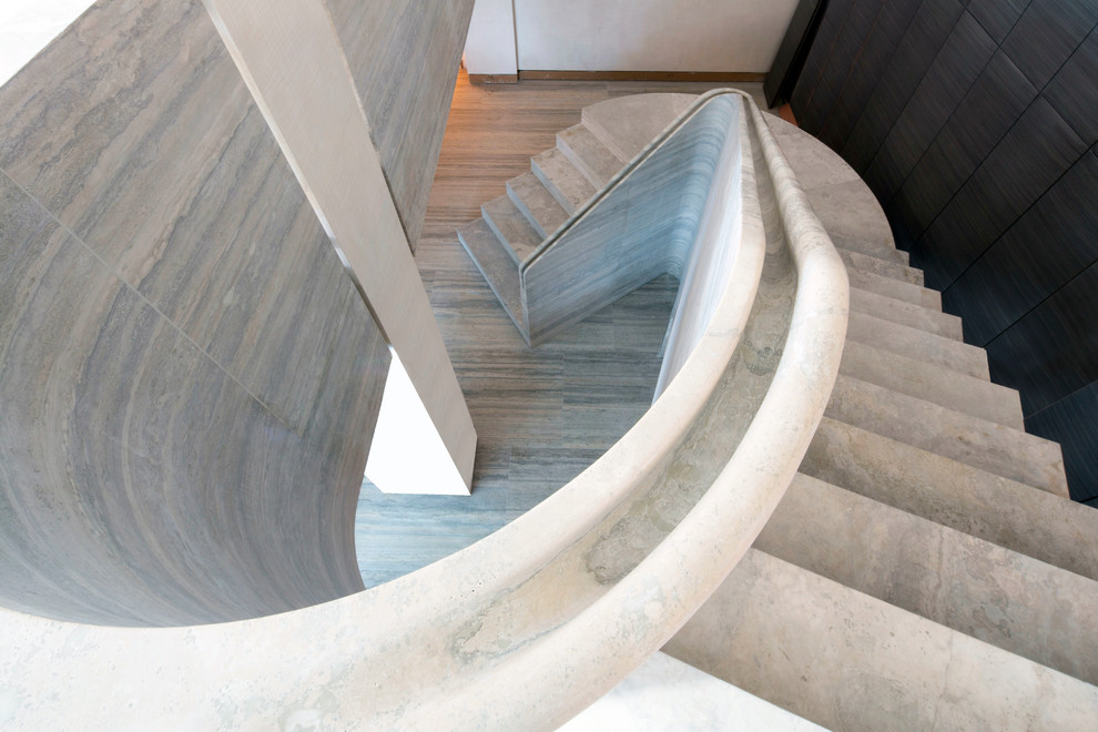 На фото: огромная изогнутая лестница в современном стиле с ступенями из известняка и подступенками из известняка