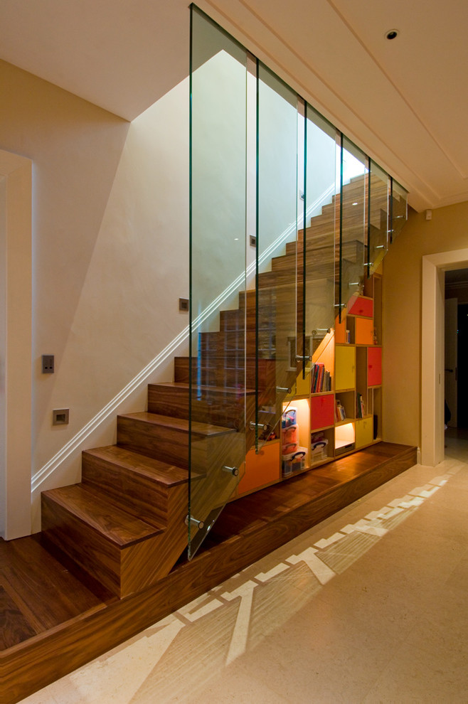 На фото: прямая деревянная лестница в современном стиле с деревянными ступенями, стеклянными перилами и кладовкой или шкафом под ней