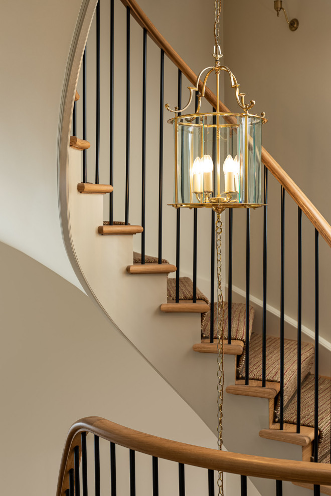Design ideas for a large traditional wood curved metal railing staircase in London with wood risers.