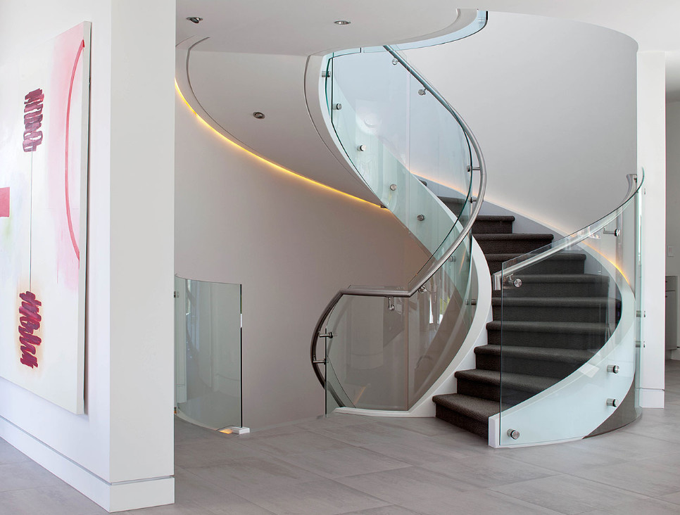 Ejemplo de escalera curva minimalista grande con escalones enmoquetados, contrahuellas enmoquetadas y barandilla de vidrio