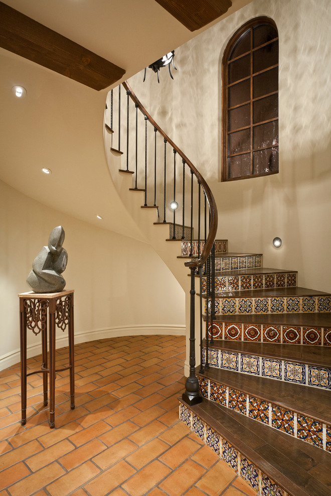 Diseño de escalera curva mediterránea con escalones de madera, contrahuellas con baldosas y/o azulejos y barandilla de metal