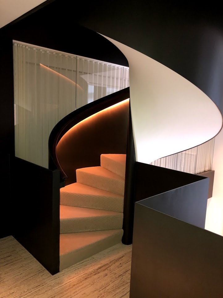 Cette image montre un grand escalier courbe minimaliste avec un garde-corps en bois, des marches en moquette et des contremarches en moquette.