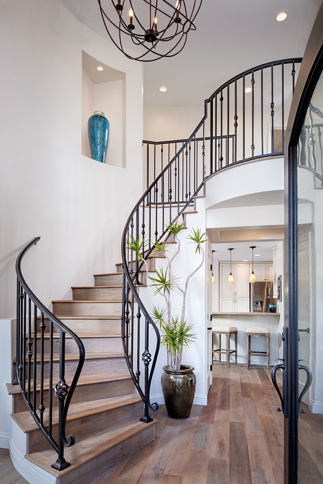 Стильный дизайн: большая изогнутая деревянная лестница в средиземноморском стиле с деревянными ступенями - последний тренд