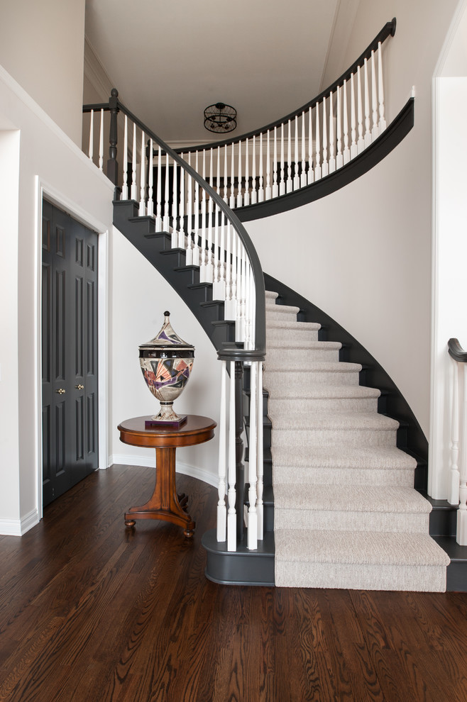 Идея дизайна: изогнутая лестница среднего размера в стиле неоклассика (современная классика) с ступенями с ковровым покрытием, ковровыми подступенками и деревянными перилами