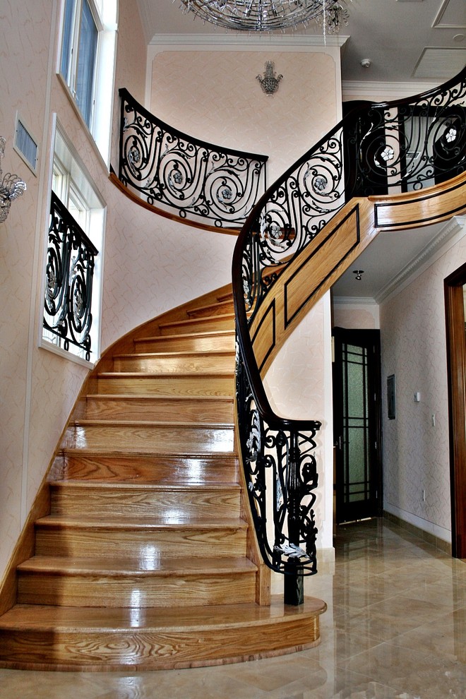 Идея дизайна: большая изогнутая деревянная лестница в классическом стиле с деревянными ступенями и металлическими перилами