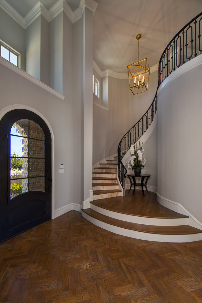 Diseño de escalera curva clásica renovada grande con escalones de madera, contrahuellas de mármol y barandilla de metal