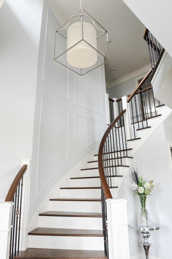 На фото: изогнутая лестница среднего размера в стиле неоклассика (современная классика) с деревянными ступенями и крашенными деревянными подступенками