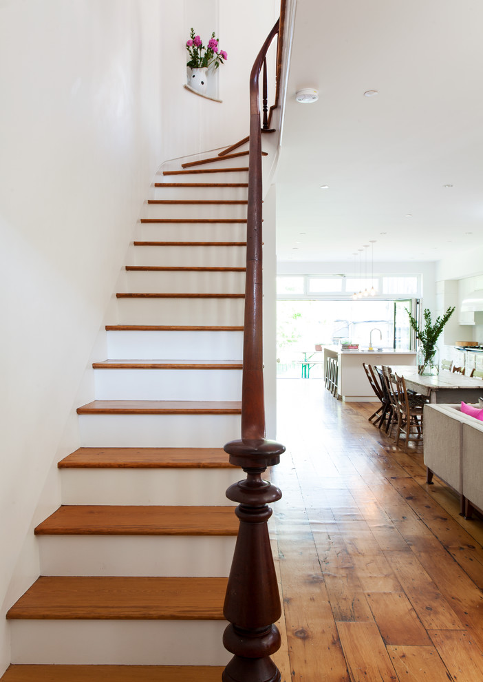 На фото: изогнутая лестница среднего размера в современном стиле с деревянными ступенями, деревянными перилами и крашенными деревянными подступенками с