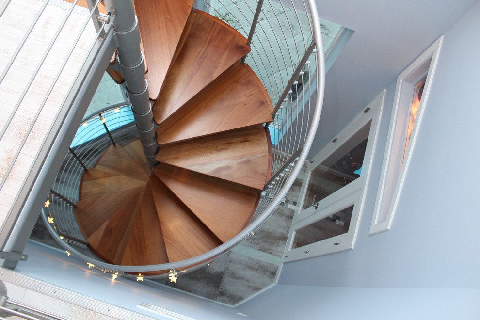 Aménagement d'un grand escalier hélicoïdal exotique avec des marches en bois, des contremarches en bois et un garde-corps en câble.