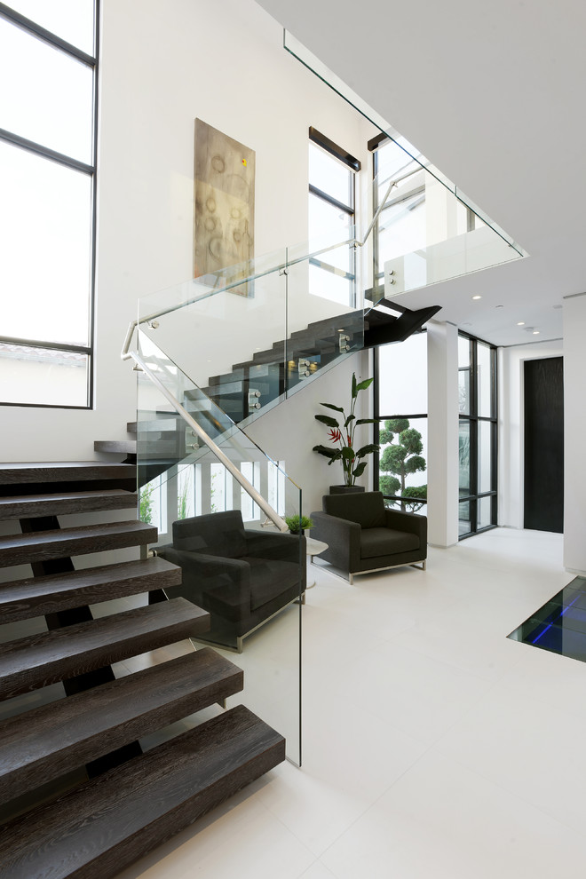 This is an example of a large contemporary wood l-shaped glass railing staircase in Los Angeles with open risers and feature lighting.