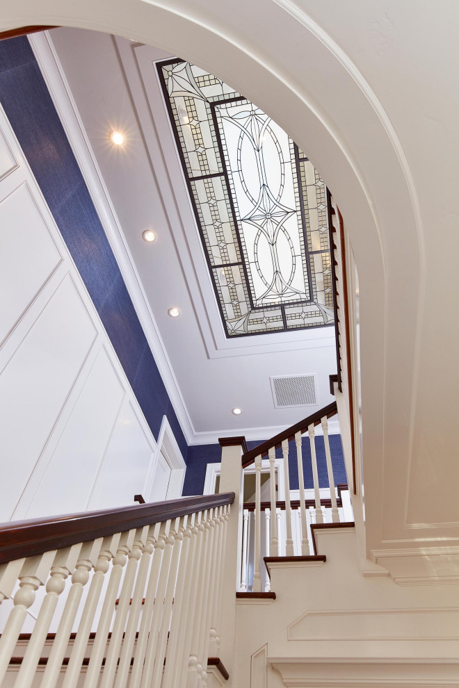 На фото: большая угловая лестница в классическом стиле с деревянными ступенями, крашенными деревянными подступенками, деревянными перилами и обоями на стенах