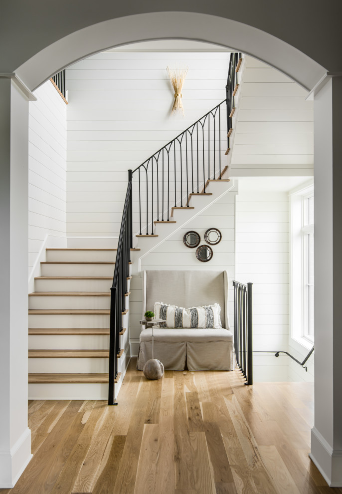 Idée de décoration pour un grand escalier peint tradition en U avec des marches en bois, un garde-corps en métal et du lambris de bois.