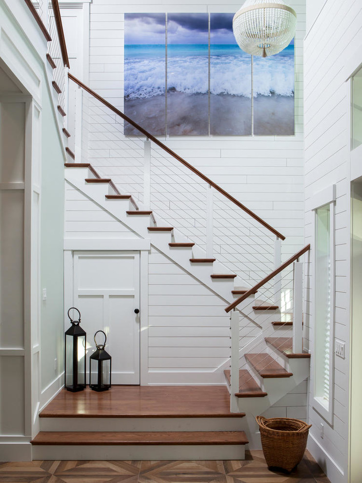 Cette photo montre un grand escalier peint bord de mer en U avec des marches en bois et un garde-corps en câble.