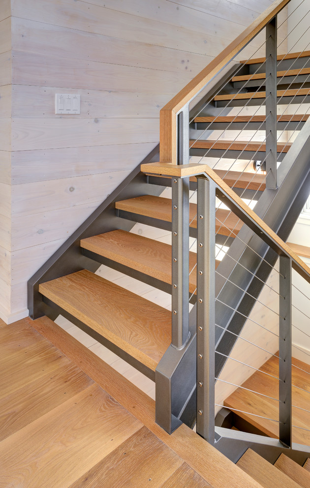 Cette image montre un escalier rustique avec des marches en bois et un garde-corps en câble.
