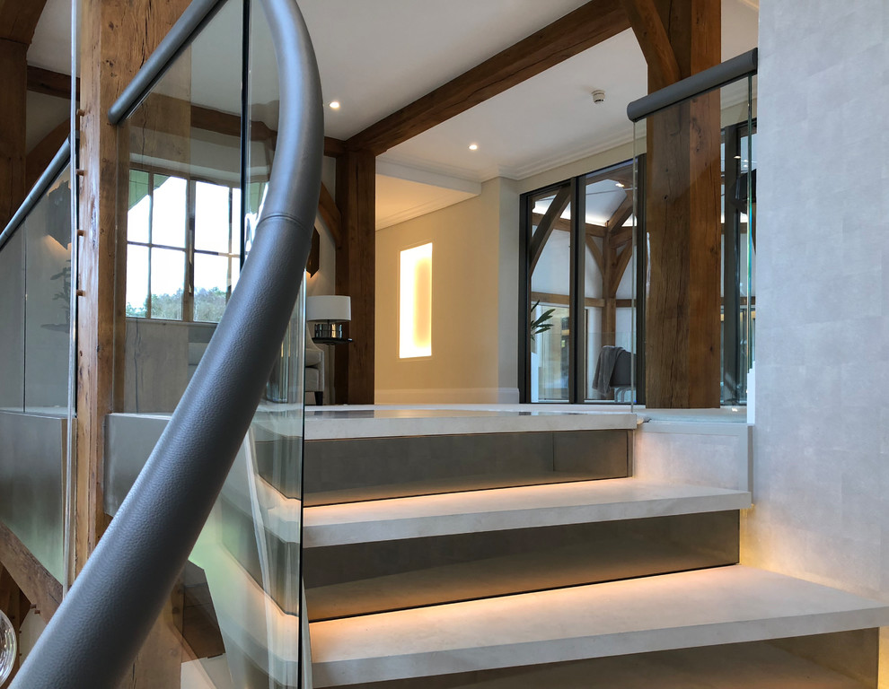 Стильный дизайн: огромная винтовая лестница в современном стиле с ступенями из известняка, подступенками из известняка и стеклянными перилами - последний тренд