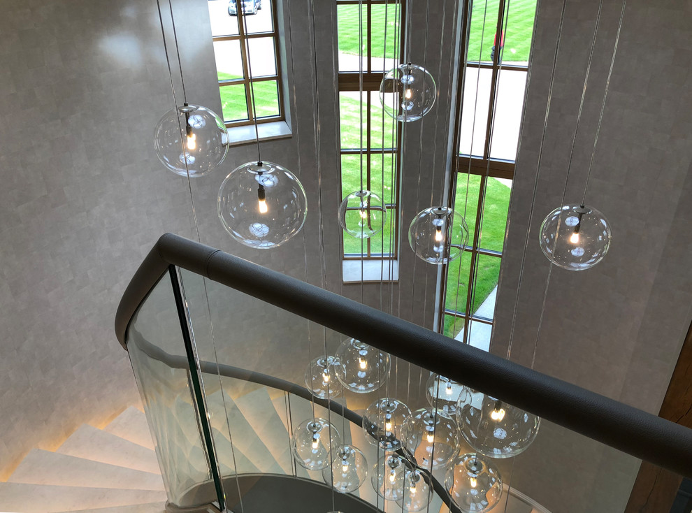 На фото: огромная винтовая лестница в современном стиле с ступенями из известняка, подступенками из известняка и стеклянными перилами