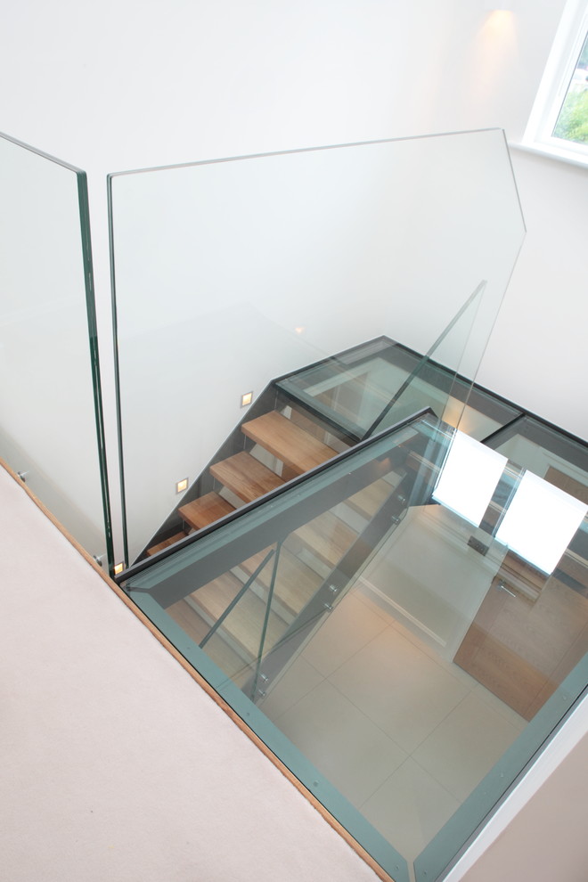 バッキンガムシャーにある高級な中くらいなコンテンポラリースタイルのおしゃれな折り返し階段 (ガラスの蹴込み板) の写真