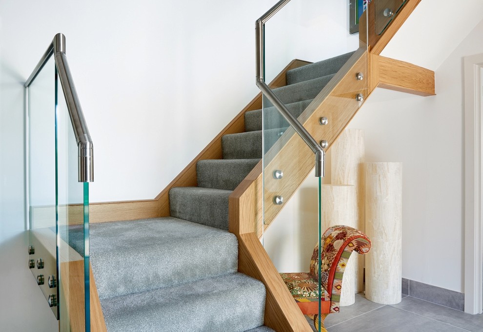 Foto på en mellanstor funkis svängd trappa, med heltäckningsmatta, sättsteg i glas och räcke i metall