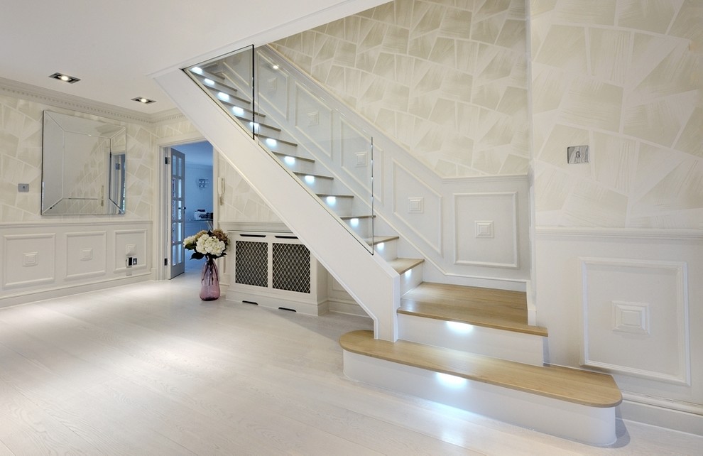 Photo of a large contemporary wood curved glass railing staircase in London with painted wood risers.