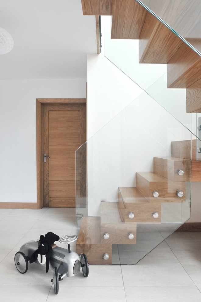 На фото: большая изогнутая лестница в современном стиле с деревянными ступенями, стеклянными подступенками и стеклянными перилами
