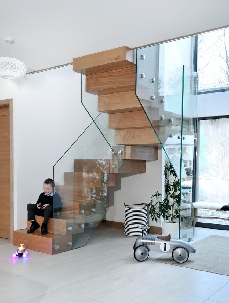 Large contemporary wood curved glass railing staircase in Cardiff with wood risers.