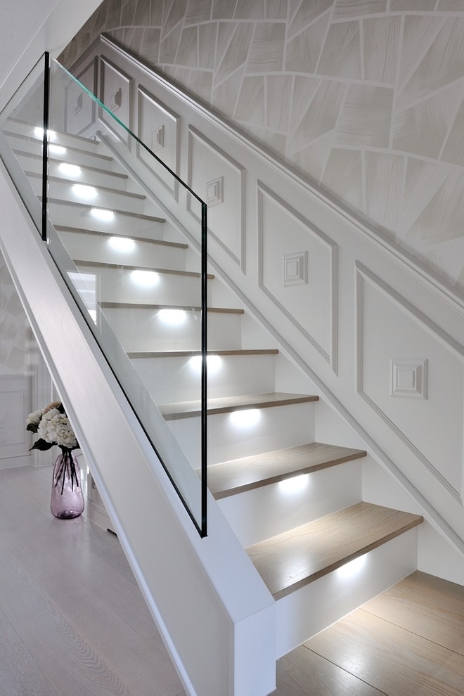 Пример оригинального дизайна: большая изогнутая лестница в современном стиле с деревянными ступенями, стеклянными перилами и крашенными деревянными подступенками