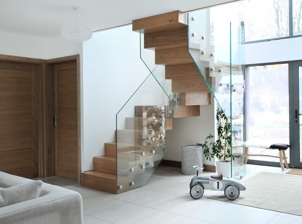 Пример оригинального дизайна: большая изогнутая деревянная лестница в современном стиле с деревянными ступенями и стеклянными перилами