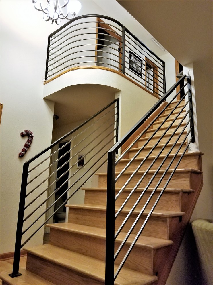 Diseño de escalera curva actual grande con escalones de madera, barandilla de metal y contrahuellas de madera
