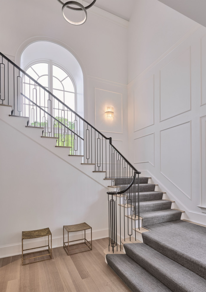 Cette photo montre un grand escalier chic en U avec des marches en moquette, des contremarches en moquette, un garde-corps en métal et boiseries.