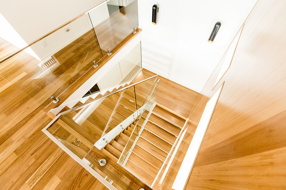 Foto på en stor funkis u-trappa i trä, med öppna sättsteg och räcke i glas