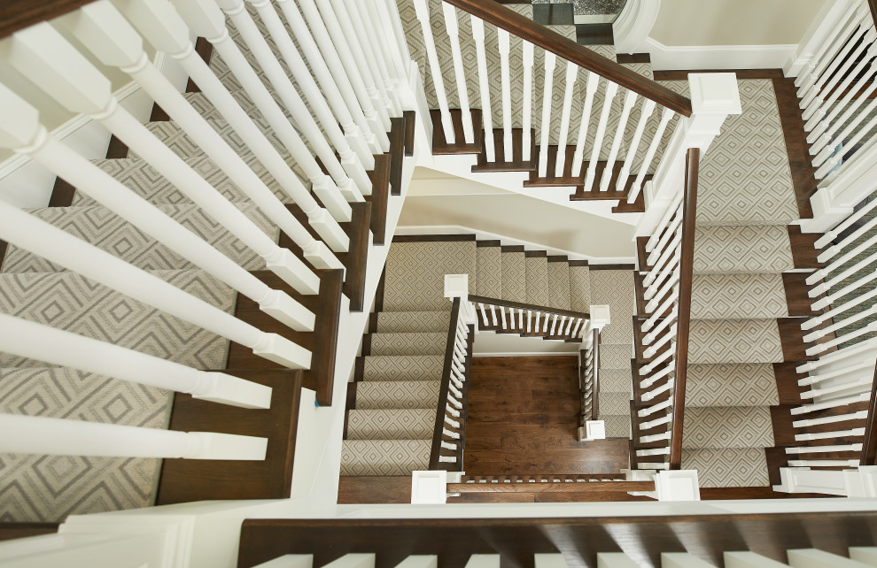 На фото: большая винтовая деревянная лестница в классическом стиле с ступенями с ковровым покрытием и деревянными перилами с