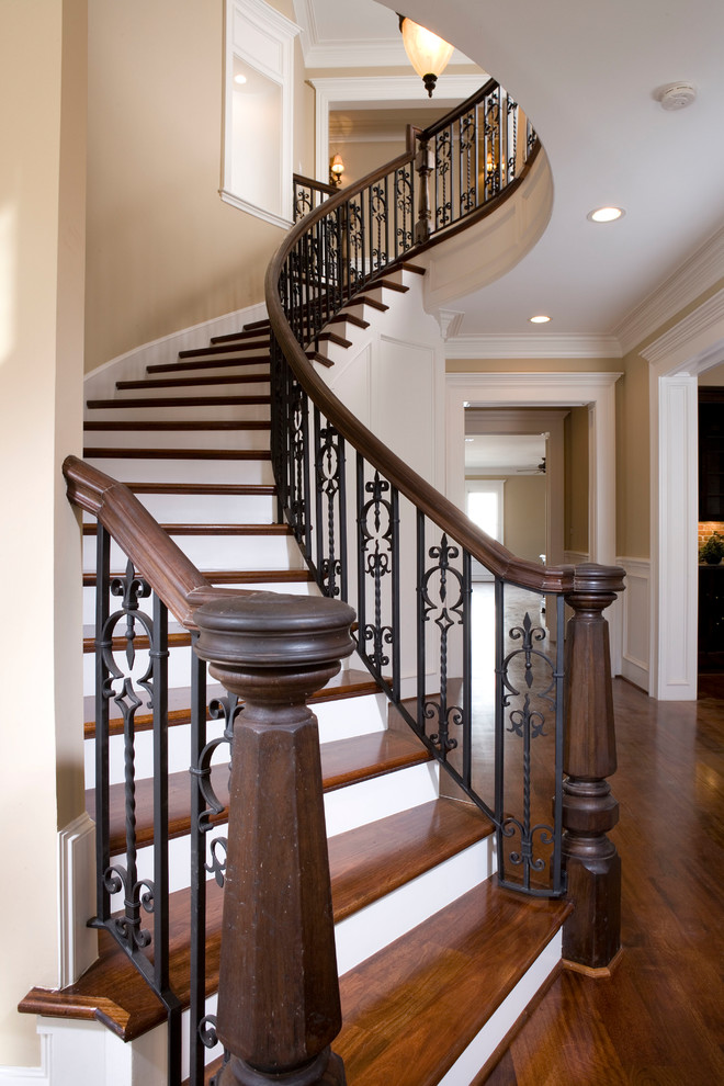 Ejemplo de escalera curva clásica grande con escalones de madera, contrahuellas de madera pintada y barandilla de metal