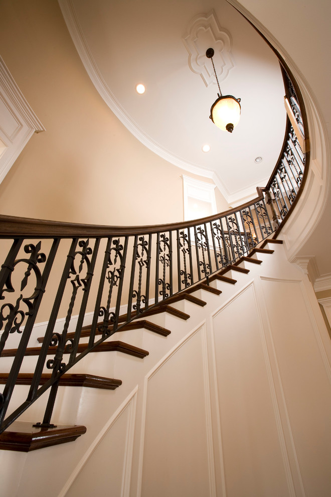 Modelo de escalera curva clásica grande con escalones de madera, contrahuellas de madera pintada y barandilla de metal