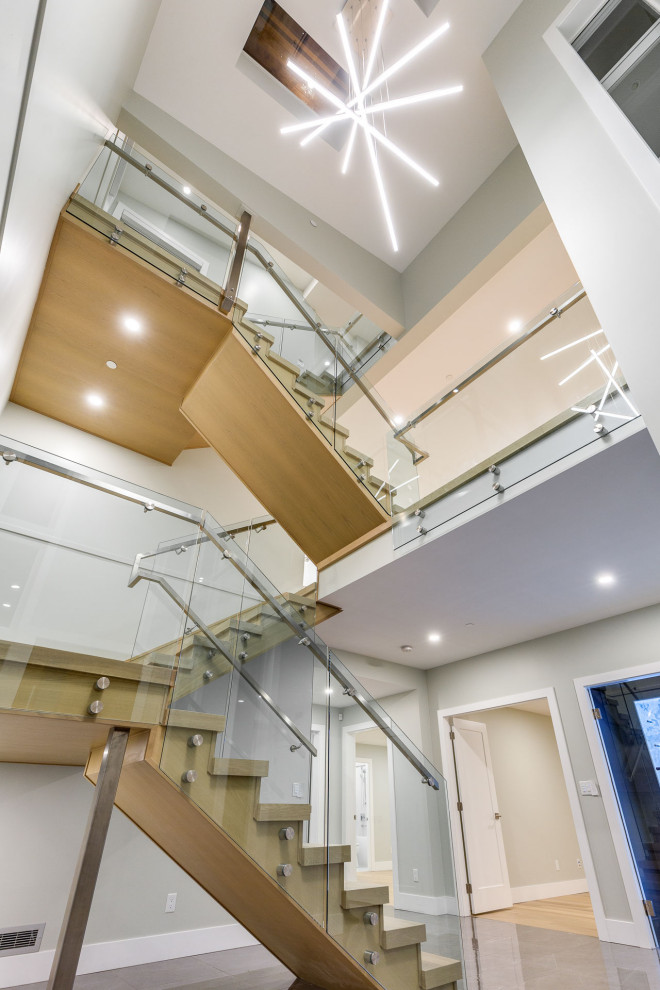 Modelo de escalera en U contemporánea grande con escalones de madera, contrahuellas de madera y barandilla de vidrio